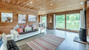 Interieur van een blokhut met houten wanden, een witte bank, een vloerkleed en een groot raam met uitzicht op een natuurlandschap.