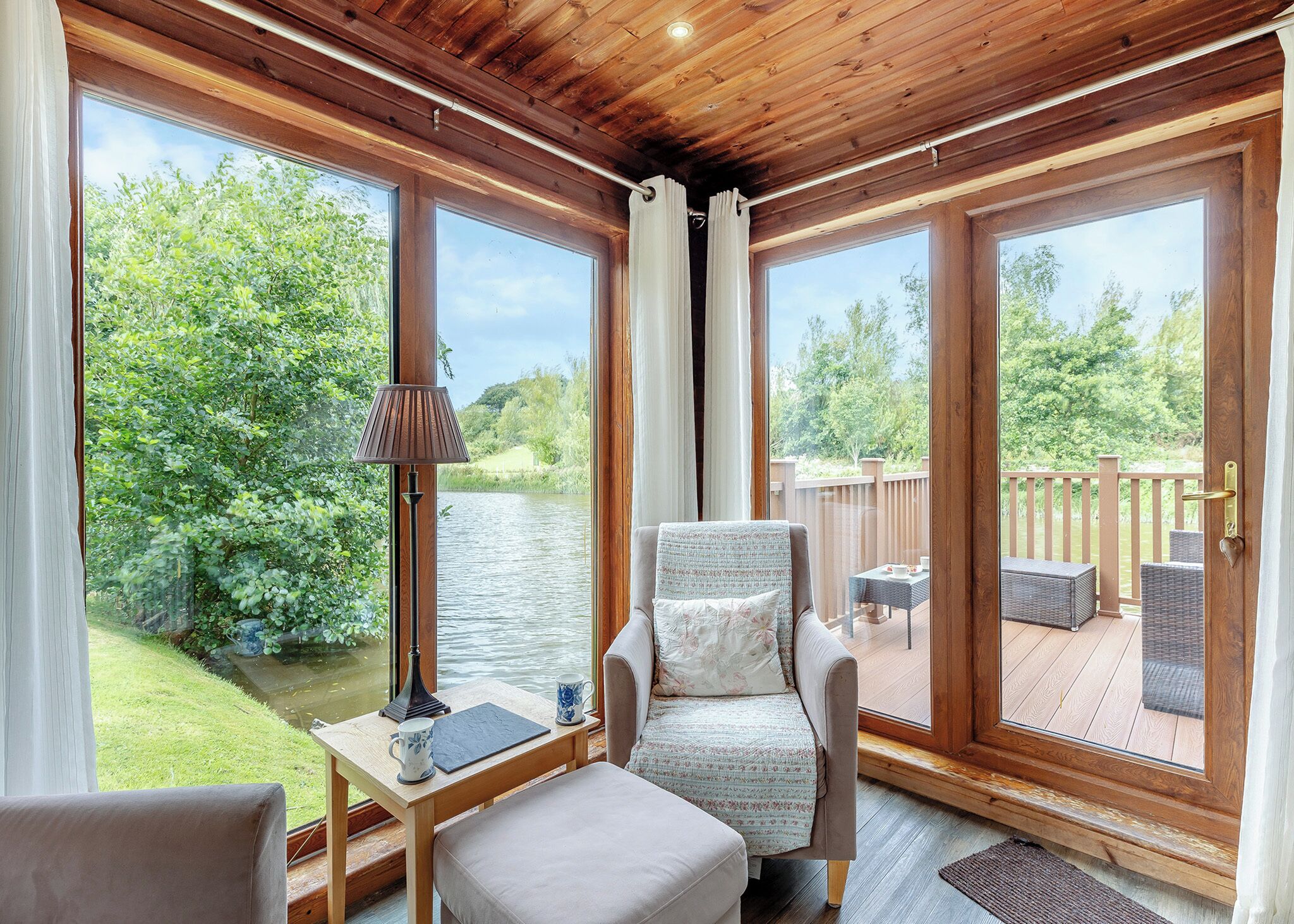 Una habitación con vista al río, una silla, una mesa con lámpara y una terraza exterior.