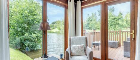 Una habitación con vista al río, una silla, una mesa con lámpara y una terraza exterior.
