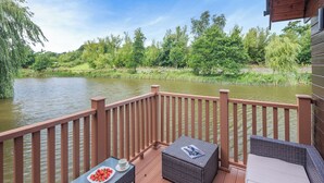 A wooden deck with a table and chairs, overlooking a body of water and greenery. - Superb lodge perched on the lake, perfect for romantic breaks. (Anglesey)