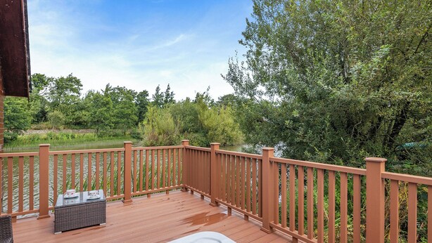 Een houten terras met een jacuzzi, een tafel met bekertjes en uitzicht op een rivier en bomen.