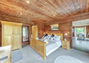 Quarto de cabana de madeira com cama, mesas de cabeceira, cômoda e um espelho grande.