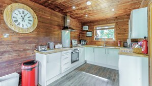 A wooden cabin interior with a kitchen featuring white cabinets, a wooden ceiling, and a large wall clock. - Superb lodge perched on the lake, perfect for romantic breaks. (Anglesey)
