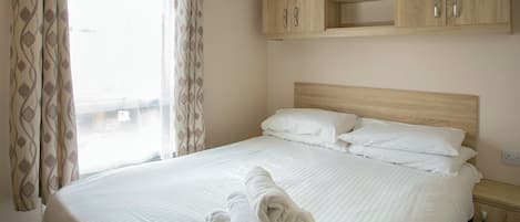 Una habitación de hotel con cama, armario de madera y ventana con cortinas.