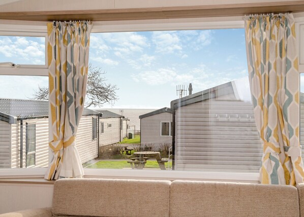 A view from a window with patterned curtains, looking out to a caravan park with multiple caravans and a picnic table.