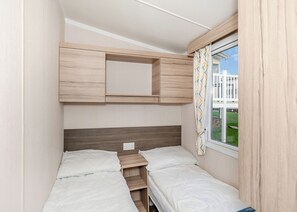 A compact bedroom with a bed, a small desk, and a window with curtains.