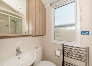 A bathroom with a sink, mirror, toilet, and a window with a caution sign.