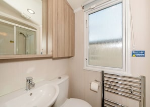 Une salle de bain équipée d’un lavabo, d’un miroir, de toilettes et d’une fenêtre sur laquelle est apposé un panneau d’avertissement.
