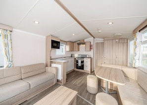 Ein kompaktes Wohnmobil-Interieur mit Küchenzeile, einer Sitzecke, einem Esstisch und einem kleinen Hocker.