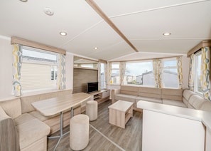 A caravan interior with a sofa, table, ottoman, and a TV.