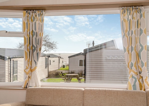 A view from a window with patterned curtains, looking out to a caravan park with multiple caravans and a picnic table.