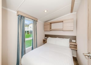 A bedroom with a bed, a window with curtains, a headboard, and built-in wooden storage.