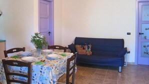 A dining area with a table set for four, a sofa, and a door with a purple frame. - LE CASTELLA RESIDENCE APP. 7 (Santa Domenica)