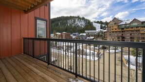 En træterrasse med gelænder i sort, der giver udsigt over et skiområde med bygninger og et sneklædt bjerg i baggrunden.