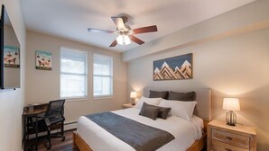 A bedroom with a bed, desk, chair, nightstands, and a ceiling fan. - Fraser Crossing/Founders Pointe, Condo 1 Bedroom w/Kitchenette Premium Unit 4547 (Winter Park)
