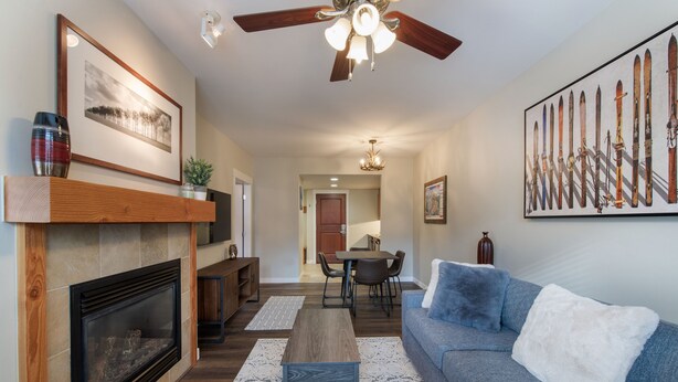 A living room with a fireplace, a sofa, a coffee table, and a dining area with chairs and a table. - Fraser Crossing/Founders Pointe, Condo 1 Bedroom w/Kitchenette Premium Unit 4547 (Winter Park)