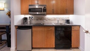 Une cuisine compacte avec des meubles en bois, un four à micro-ondes en acier inoxydable, un lave-vaisselle et un évier.