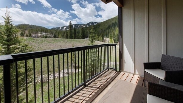 Un balcon offrant une vue sur un paysage montagneux, une terrasse en bois et un canapé en osier.