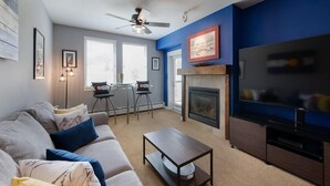 Un salon comprenant un canapé, une table basse, une cheminée, un téléviseur et un ventilateur de plafond.