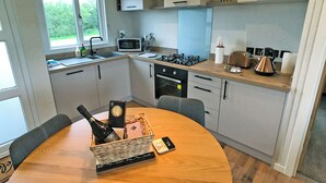 Eine kompakte Küche mit Mikrowelle, Herd und Spüle. Ein Esstisch mit Stühlen und eine Flasche Champagner sind vorhanden.