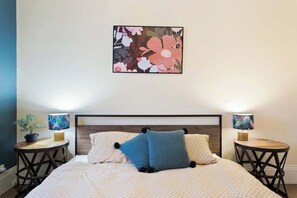 A bed with a patterned bedspread, two pillows, a wall-mounted floral artwork, and two bedside tables with lamps.