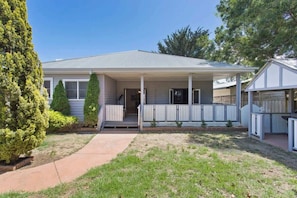 A single-story house with a front porch, a covered entryway, and a small front yard with grass and a tree.