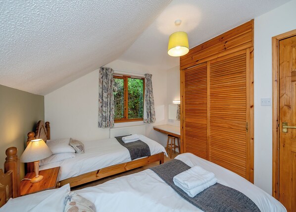 Une chambre avec deux lits, une armoire en bois, un bureau avec une chaise, une fenêtre avec des rideaux et un luminaire au plafond.