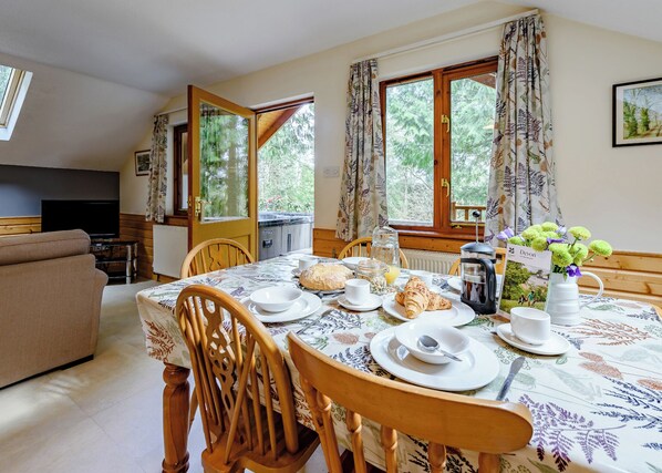 A dining area with a table set for breakfast, chairs, a television, and a view of greenery outside.