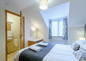 A bedroom with a bed, a bedside table, a window with curtains, a door leading to a bathroom, and a ceiling light. - 3 bedroom accommodation in Webbery, Bideford (Webbery, Bideford)
