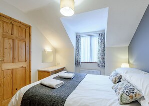 A bedroom with a bed, a wooden wardrobe, a nightstand, a window with curtains, and a ceiling light.