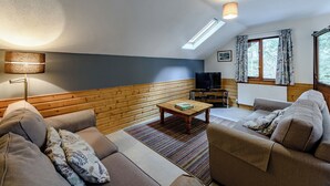 A cozy living room with a sofa, a coffee table, a television, and a window with curtains. - 3 bedroom accommodation in Webbery, Bideford (Webbery, Bideford)