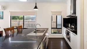 Une cuisine moderne dotée d’un îlot central, d’appareils électroménagers en acier inoxydable et de luminaires suspendus.