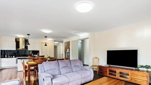 Un salon moderne comprenant un canapé, un téléviseur, un meuble en bois et un coin repas avec des chaises et une table.