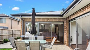 Un jardin avec un barbecue, un espace salon extérieur et une porte-fenêtre coulissante donnant sur le salon.