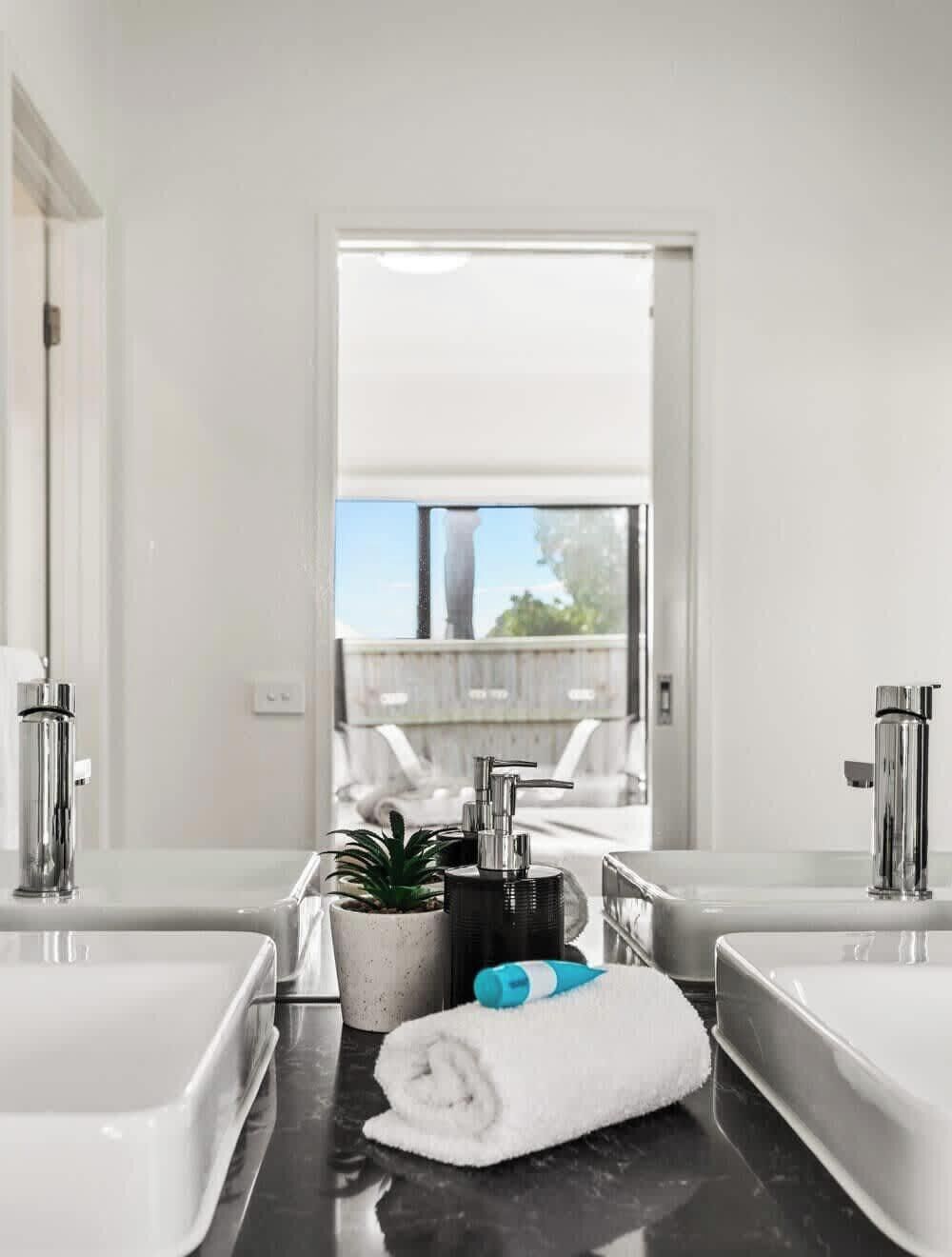 A modern bathroom with two sinks, a potted plant, and a towel on the counter.