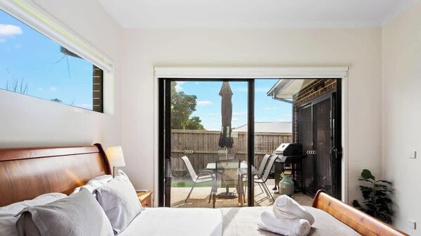 A bedroom with a bed, a nightstand, a lamp, and a view of an outdoor patio with a table and chairs. - Modern Family Home w/ Large Backyard & Fast WiFi (Cowes)