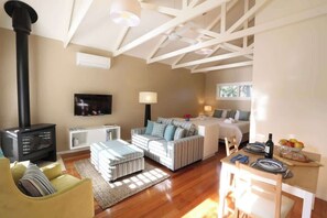 A cozy living room with a fireplace, a sofa, a TV, and a dining area with a table set for two. - Driftwood - Spa Cottage for Two (Cowes)