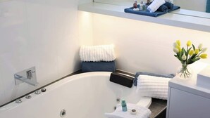 Une salle de bain moderne avec une baignoire sur pieds, un miroir au-dessus du lavabo et un petit vase avec des fleurs posé sur le comptoir.