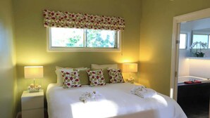 Quarto de hotel com uma cama, duas luminárias de cabeceira, uma janela com cortina florida e um espelho.
