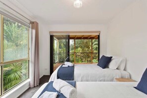 A room with two beds, a large window, and a view of greenery.