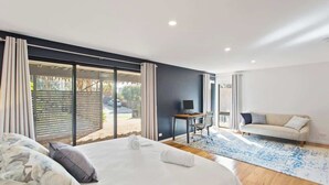 A bedroom with a large bed, a desk, a sofa, and a view of the outdoors.