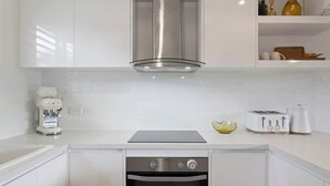 Een kleine keuken met witte kasten, een ingebouwde oven, een roestvrijstalen afzuigkap, een koffiezetapparaat en een broodrooster.
