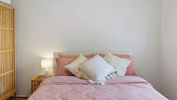 Een slaapkamer met een bed, kussens, een nachtkastje en een houten garderobe.