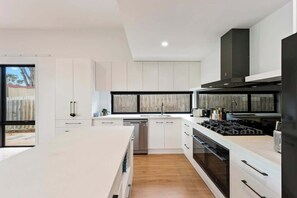 A modern kitchen with white cabinetry, a central island, and a built-in oven. - Upscale Family Retreat Just 5 Min Walk to Beach (Cape Woolamai)