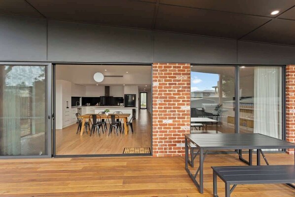 Una cocina moderna con zona de comedor, grandes puertas correderas de vidrio que dan a un espacio exterior y suelo de madera.