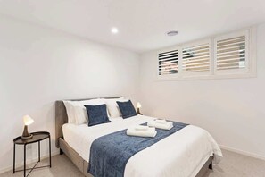 A bedroom with a bed, bedside lamps, a window with blinds, and a carpeted floor. - Upscale Family Retreat Just 5 Min Walk to Beach (Cape Woolamai)