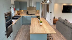 A modern kitchen with a central island, built-in oven, and a dining area with a grey sofa. - Experience the ultimate retreat in this stunning woodland lodge. (Chipping)