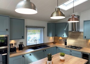 A modern kitchen with blue cabinets, a wooden countertop, a built-in stove, and pendant lighting.