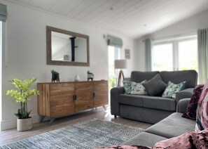 A living room with a grey sofa, a wooden cabinet, a mirror, and a floor lamp.