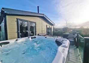 A hot tub on a wooden deck with a house in the background. - Experience the ultimate retreat in this stunning woodland lodge. (Chipping)